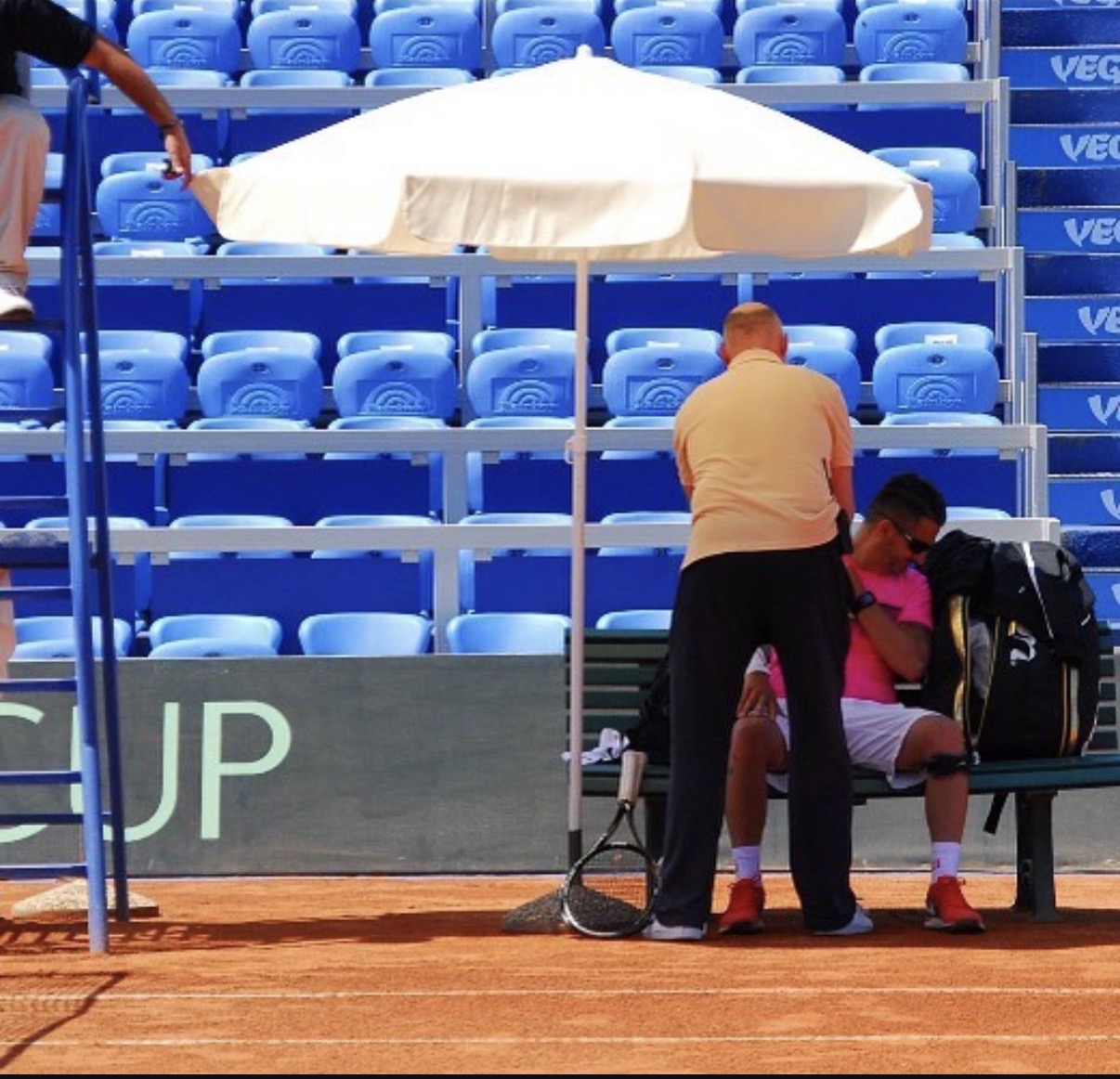Trainer betreut Spieler auf der Bank mit Sonnenschirm beim Davis Cup
