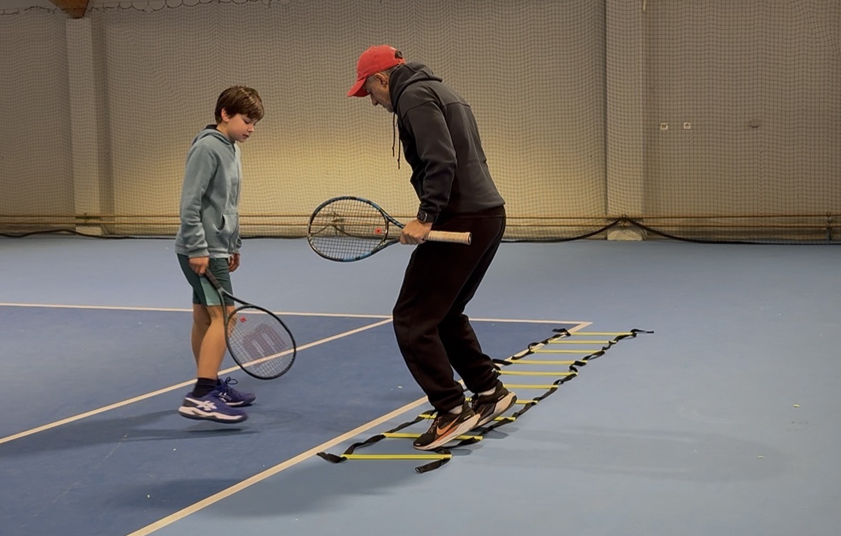 Trainer demonstriert Koordinationsleiter-Übung mit Kind in der Tennishalle