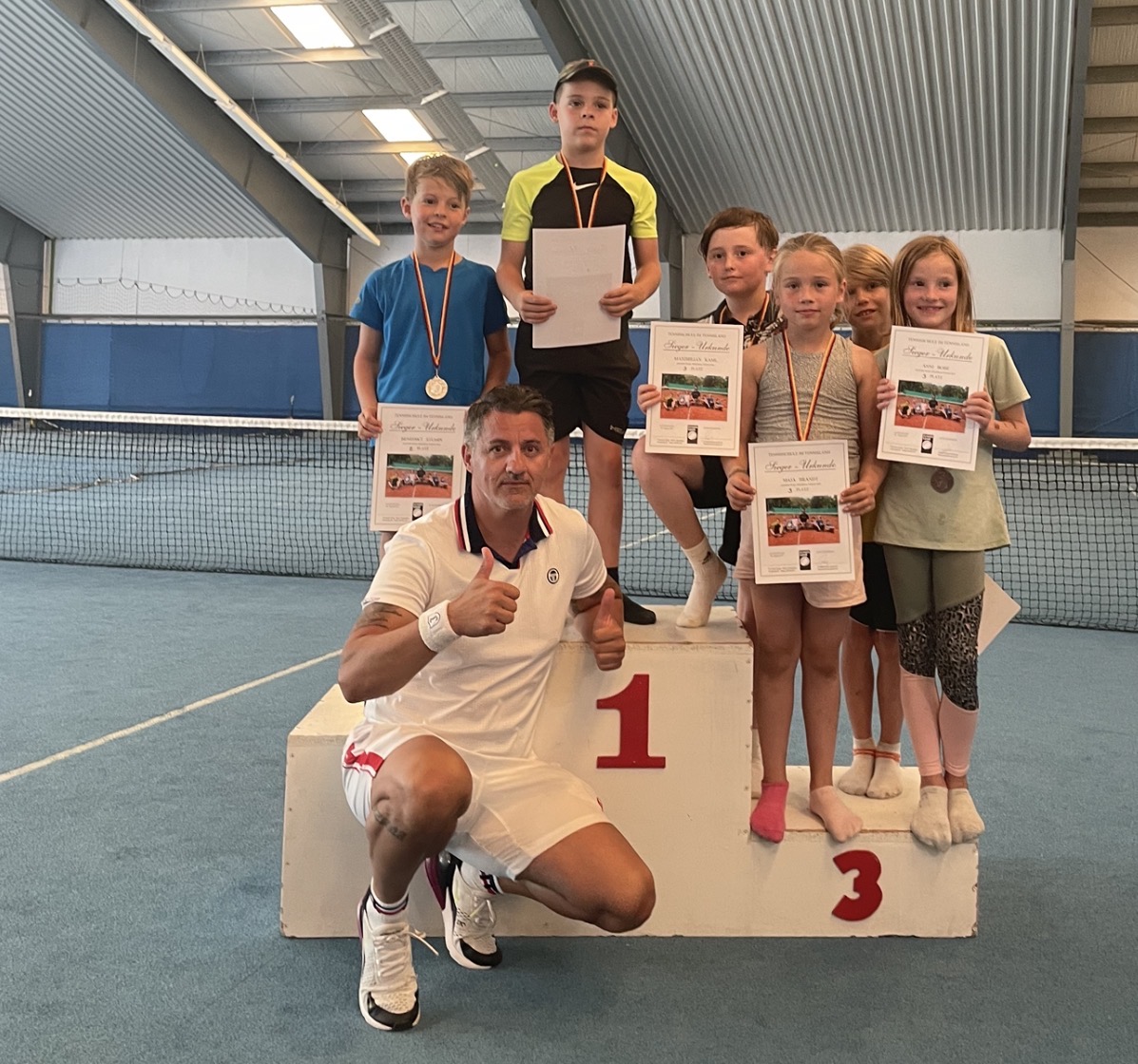 Trainer mit Daumen hoch vor Kindern auf dem Siegerpodest in der Tennishalle