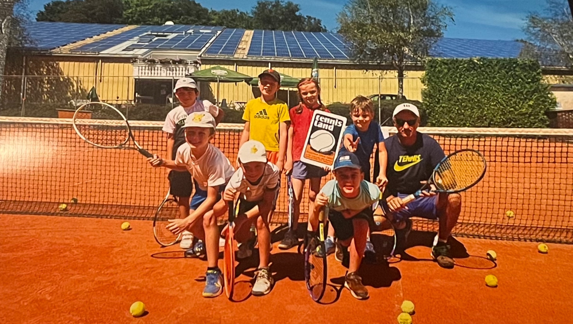 Trainer mit Kindergruppe und Tennisland-Schild auf Sandplatz