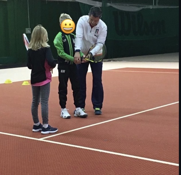 Trainer zeigt zwei Kindern den Griff am Schläger in der Tennishalle