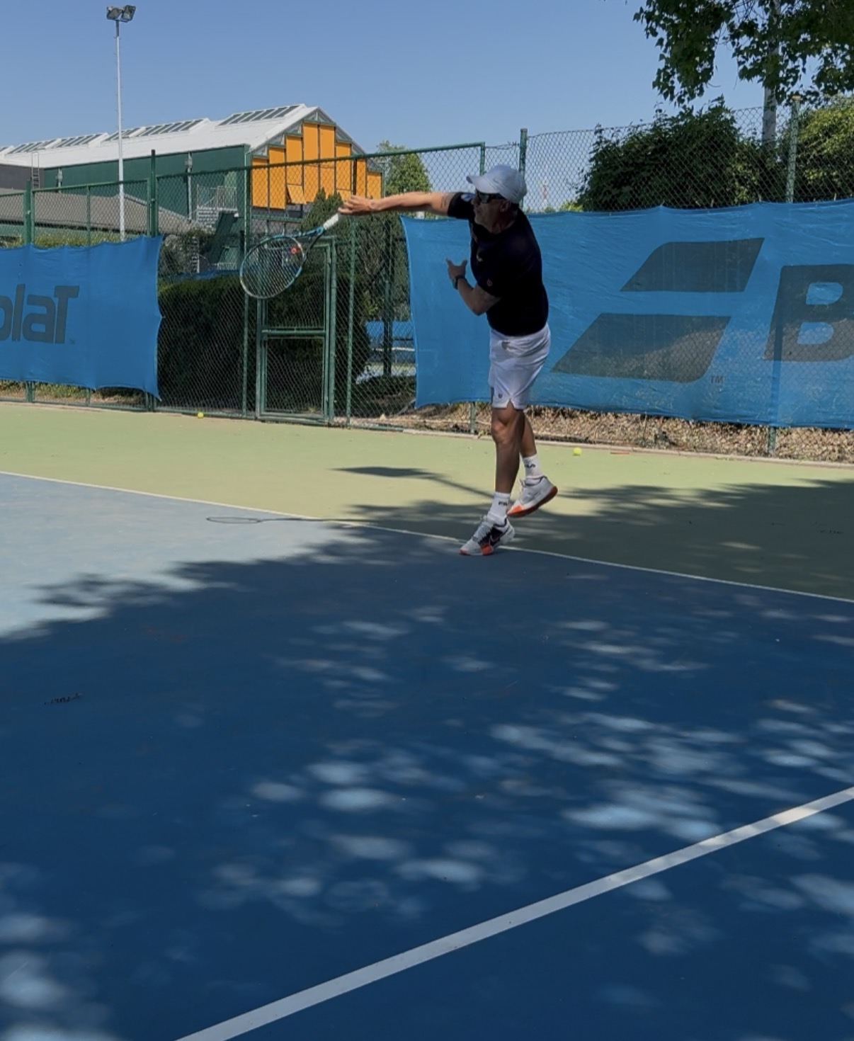 Trainer beim Aufschlag auf Hartplatz vor Babolat-Bande