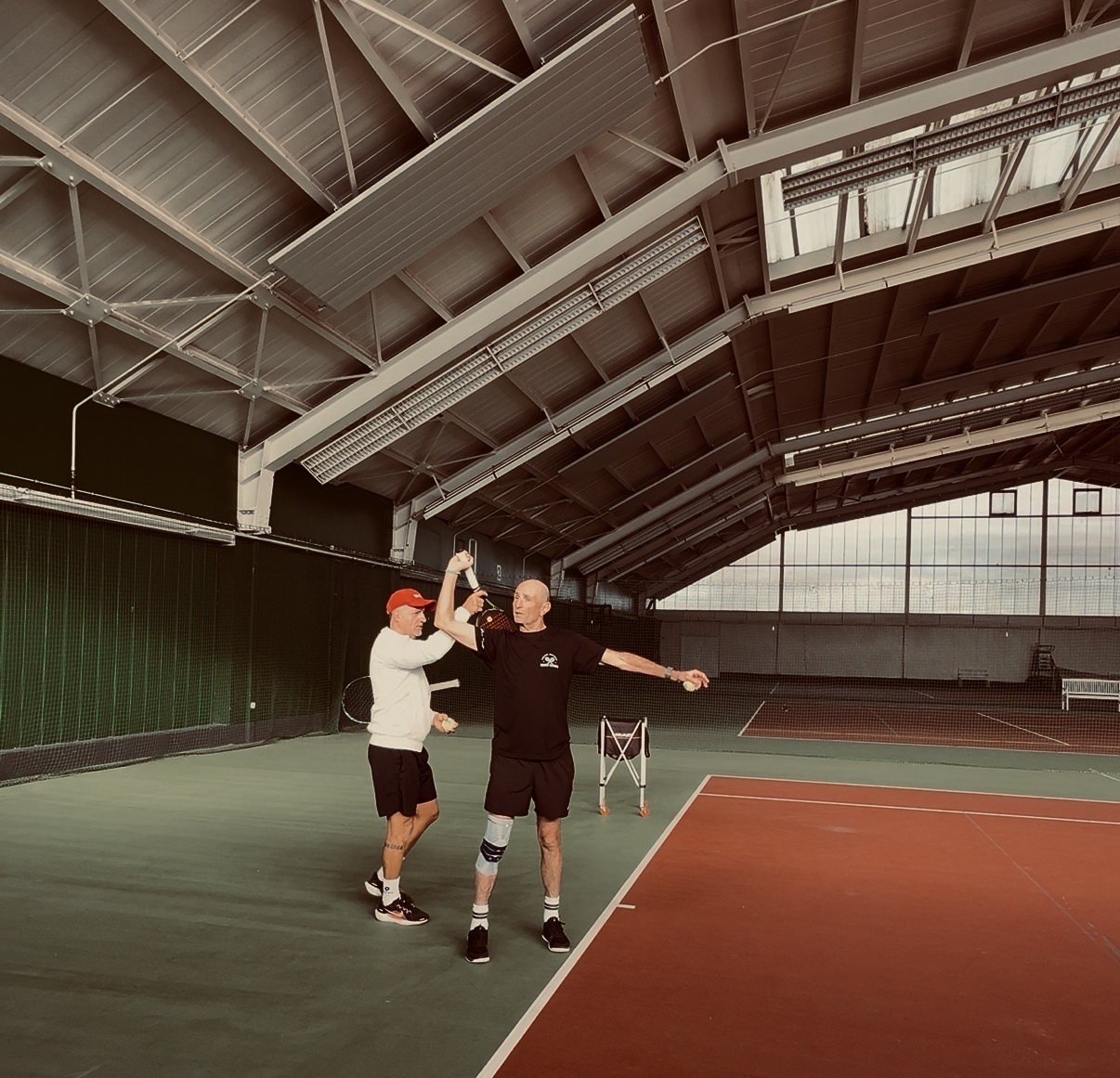 Trainer korrigiert Aufschlag-Position mit Schüler in der Tennishalle