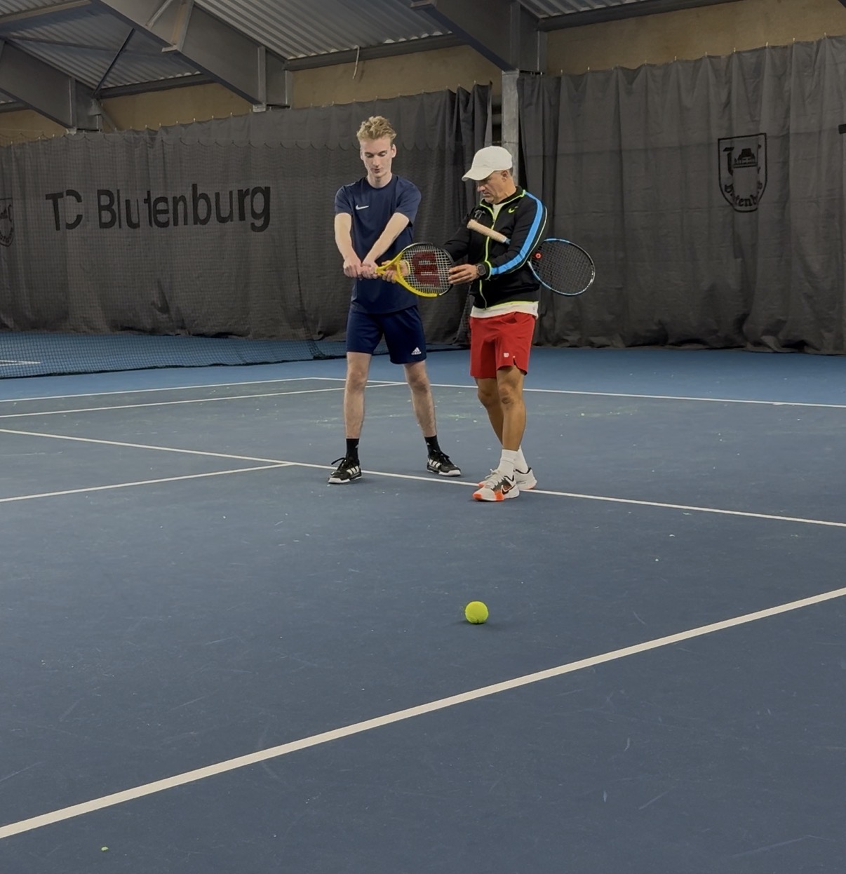 Trainer korrigiert Rückhand-Technik mit Schüler im TC Blutenburg