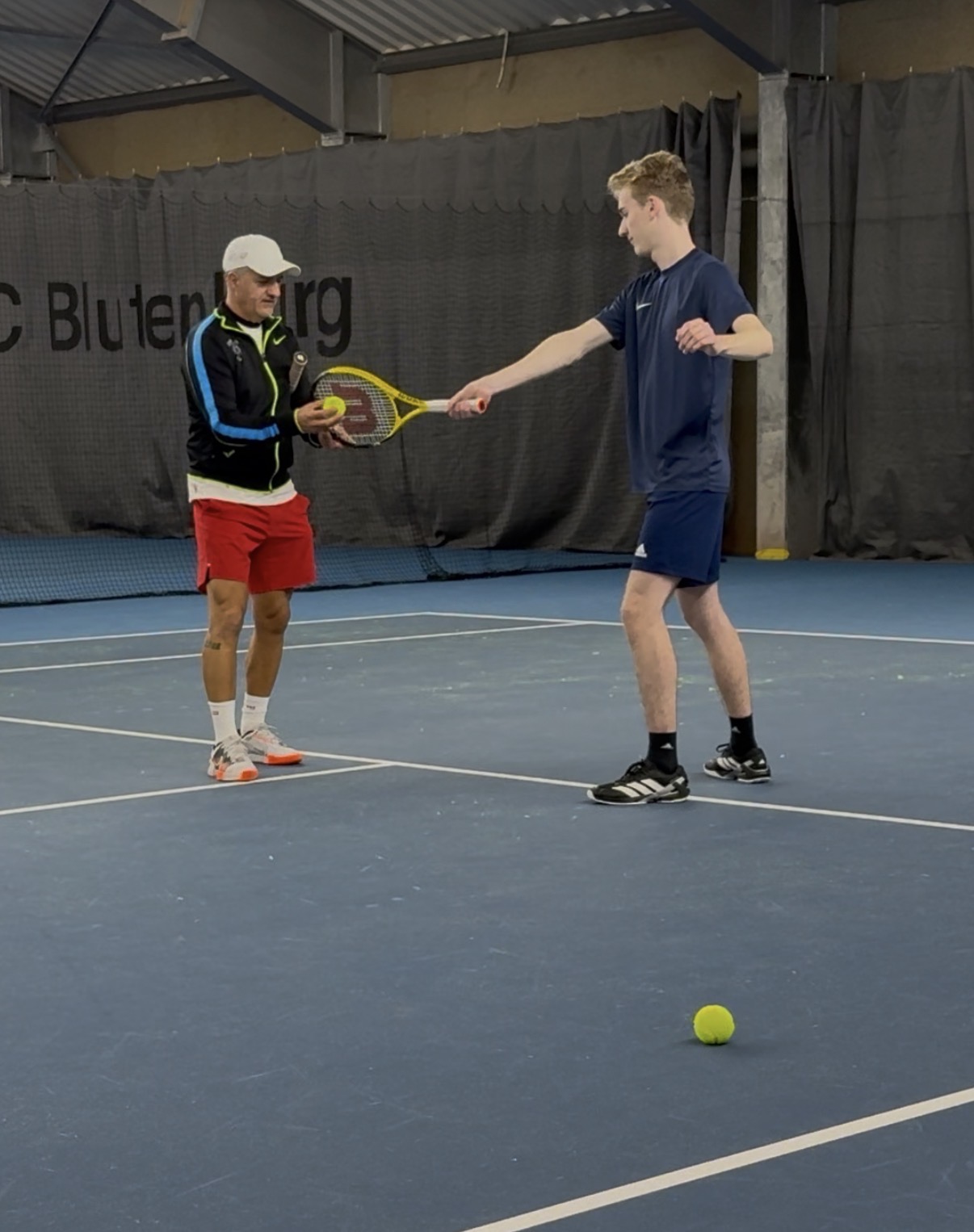 Trainer reicht Schüler einen Ball in der Tennishalle TC Blutenburg